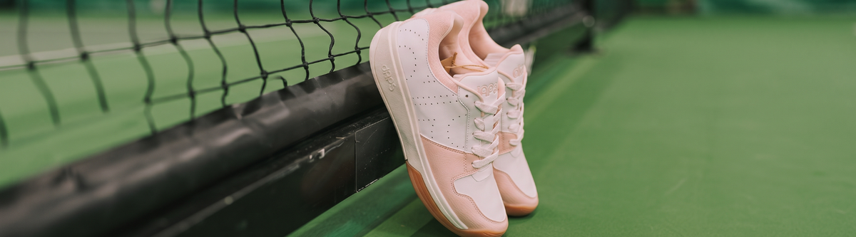 Pink pickleball shoes resting on net post