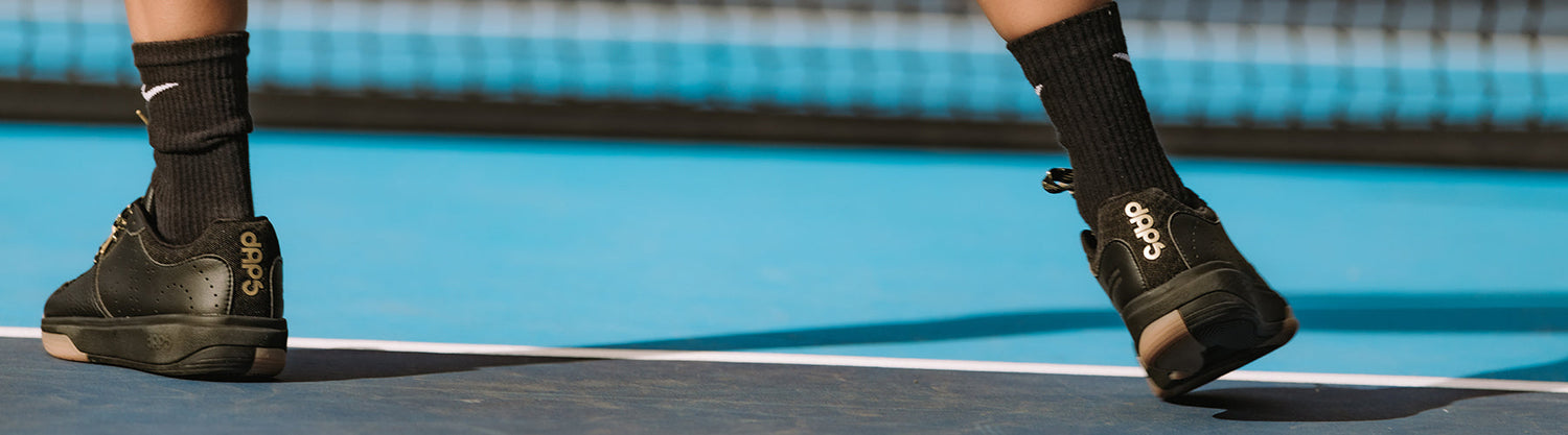 Close-up of a player wearing black DAPS court shoes on a blue pickleball court surface