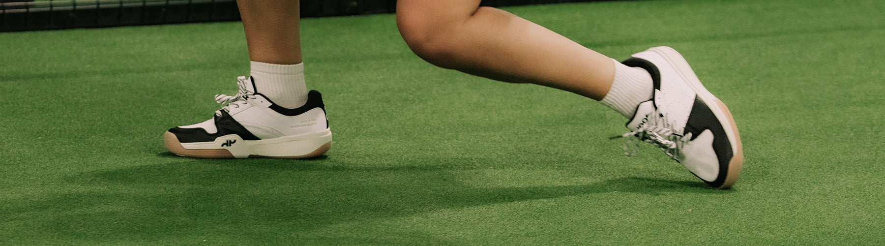 Player wearing black and white court shoes on an indoor green pickleball court surface