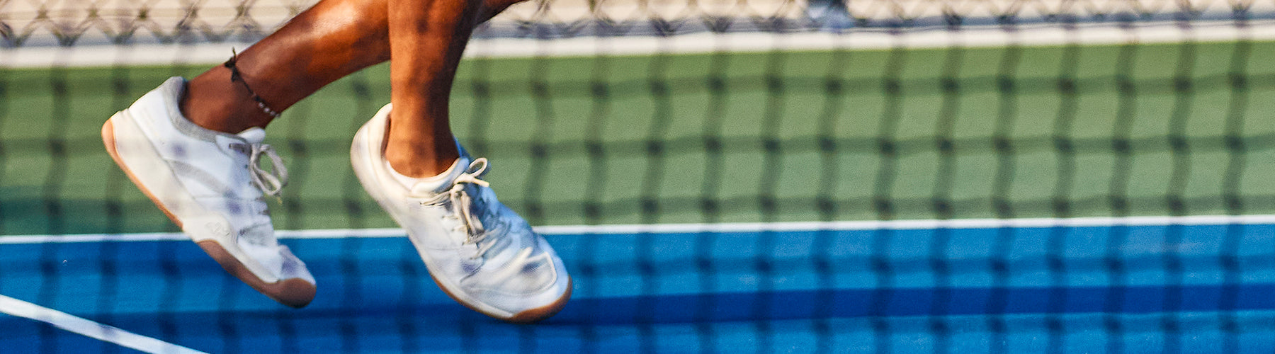 Close-up of a pickleball player mid-movement in white wide toe box shoes on a blue court, showcasing athletic footwear designed for comfort and performance.
