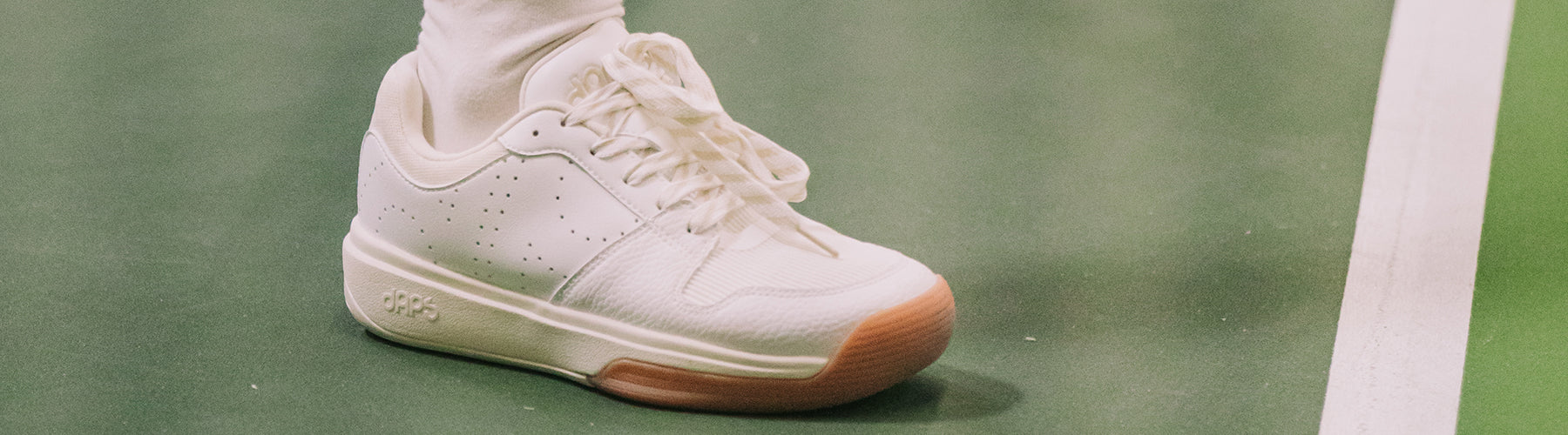 white DAPS pickleball shoe with perforated toe detailing and a gum sole, worn on an outdoor court.