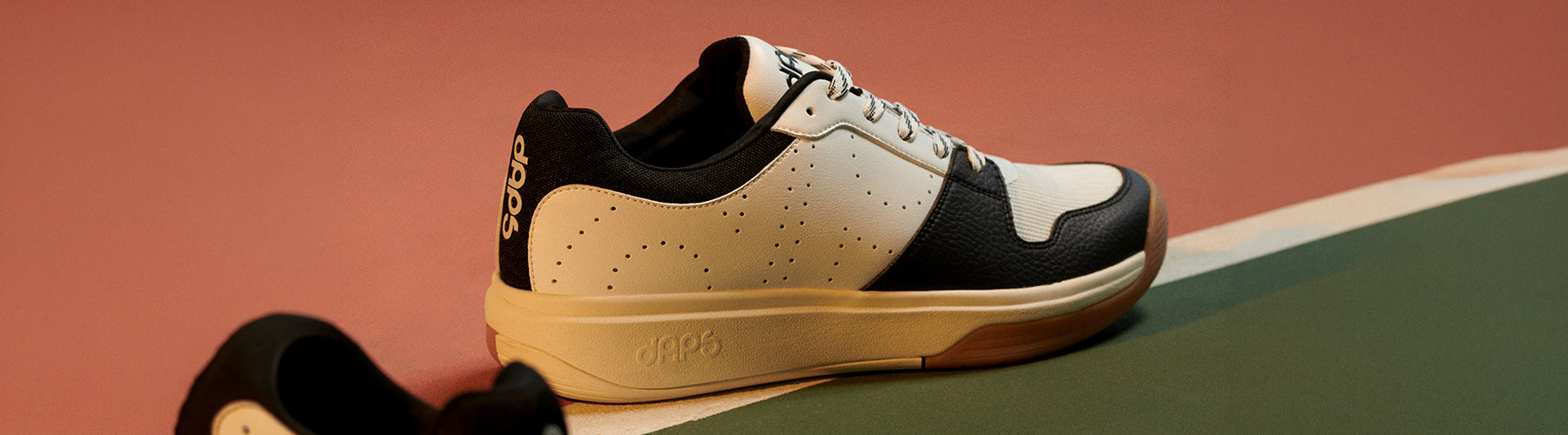 A black and white DAPS pickleball shoe with gum sole resting on a court surface, showcasing the lateral support and court-ready design.