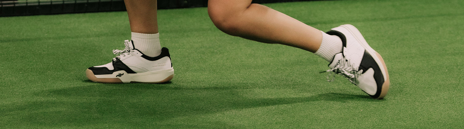 Player wearing black and white court shoes on an indoor green pickleball court surface