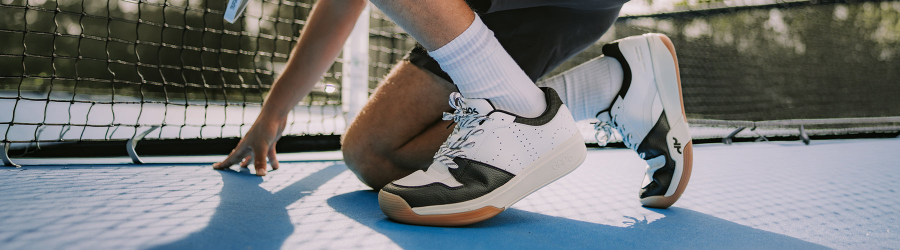 Close-up of Daps Fit wide toe pickleball shoes on a blue court surface, showing natural foot positioning and gum sole
