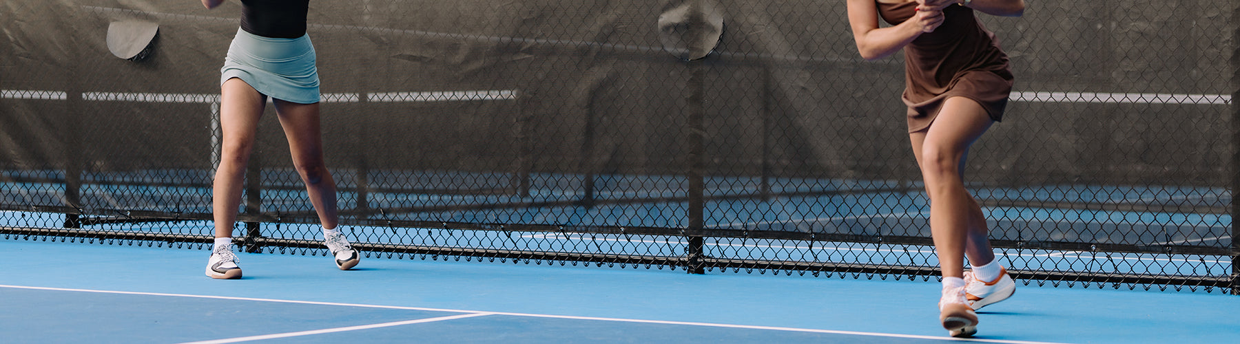 Two women playing pickleball on a blue court, wearing athletic skirts and supportive court shoes