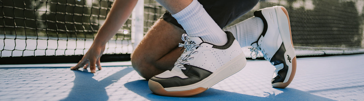Close-up of a player wearing white and black court shoes on a pickleball court near the net